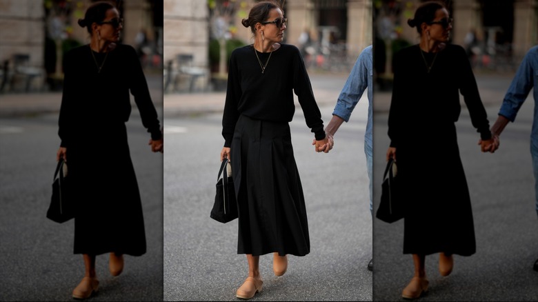 Une femme portant un pull noir rentré dans une jupe avec des mules