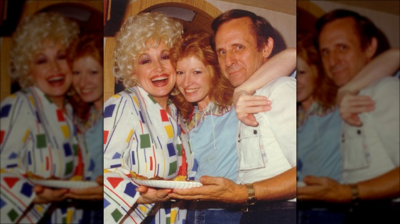 Dolly Parton (à gauche) embrasse Judy Ogle (au milieu) qui porte un haut bleu clair et un carré roux