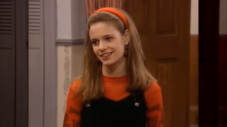Andrea Barber portant un bandeau orange, un haut orange et une salopette noire