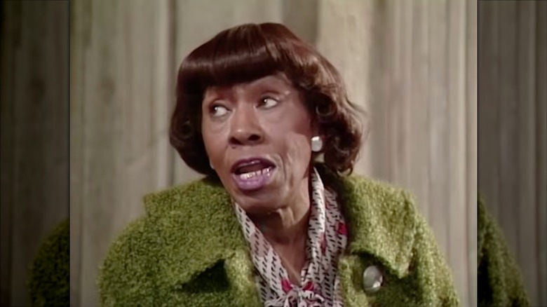 Helen Martin portant un manteau vert et un chemisier crème à motifs