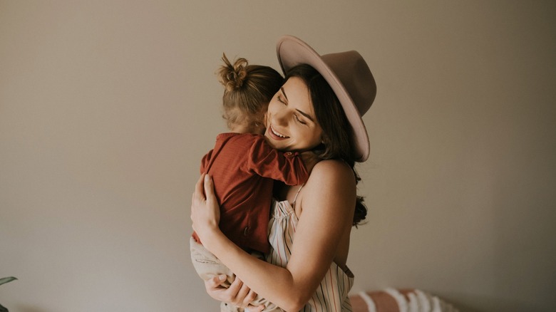 Une femme vêtue d’une tenue rustique d’inspiration occidentale tient son bébé dans ses bras.