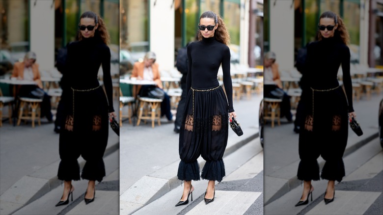 Une fille brune portant une ceinture en chaîne dorée avec un pantalon noir et un col roulé noir