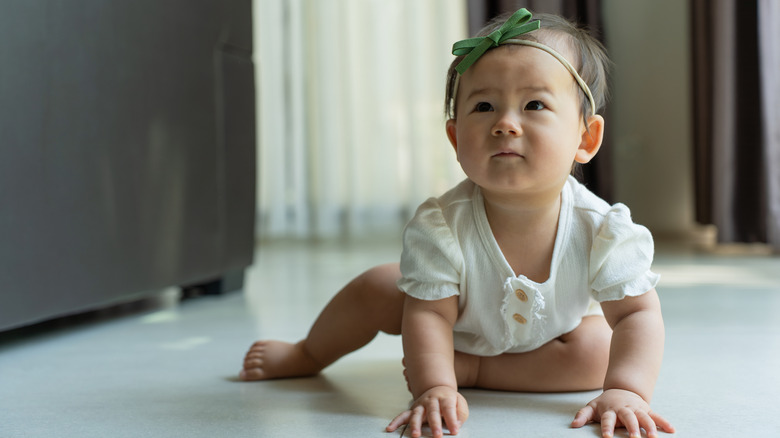 Un bébé qui rampe tout en portant un bandeau et une barboteuse blanche