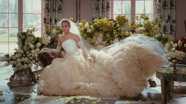 Sarah Jessica Parker dans le rôle de Carrie Bradshaw assise, vêtue d'une robe de mariée tendance et de gants.