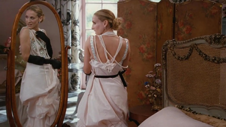 Sarah Jessica Parker dans le rôle de Carrie Bradshaw portant une robe de mariée drapée avec des gants noirs et des colliers de perles.